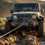 Veículo 4x4 off-road com guincho elétrico instalado no para-choque dianteiro realizando recuperação em terreno lamacento