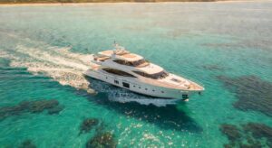 Iate de luxo branco navegando em águas cristalinas brasileiras visto de cima, mostrando design moderno e múltiplos decks