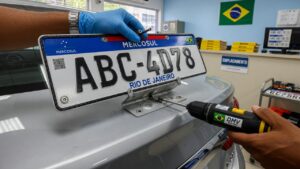 Funcionário instalando placa de licenciamento em veículo prateado em ambiente de órgão de trânsito