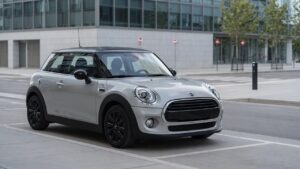 Mini One compact car front three-quarter view in urban setting, showcasing its entry-level design and 1.6 engine model