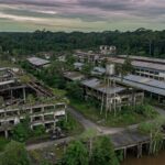 Vista aérea de complexo industrial abandonado da Ford na Amazônia com estruturas cobertas pela vegetação tropical