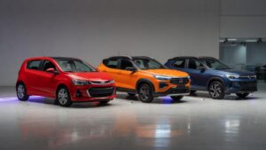 Três carros compactos - Chevrolet Sonic, Fiat Pulse e VW Tera - posicionados lado a lado em showroom automotivo para comparação