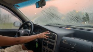 Interior de carro com vidro embaçado e motorista ajustando controles do painel para desembaçar o para-brisa