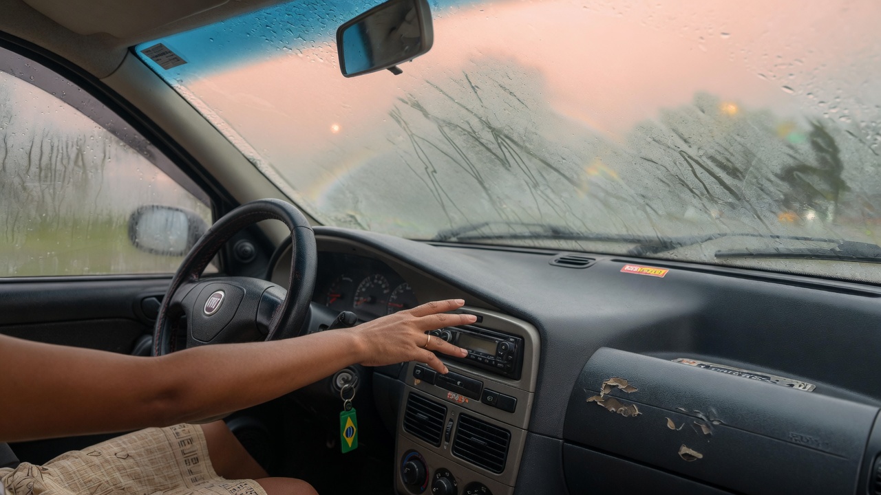Interior de carro com vidro embaçado e motorista ajustando controles do painel para desembaçar o para-brisa