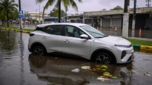 Carro elétrico parcialmente submerso em enchente urbana com água atingindo as portas do veículo