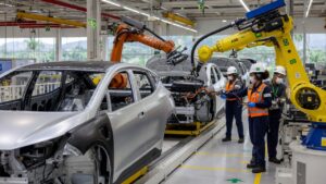 Modern automotive assembly line showing electric vehicle production in Brazilian manufacturing plant with robotic automation and workers