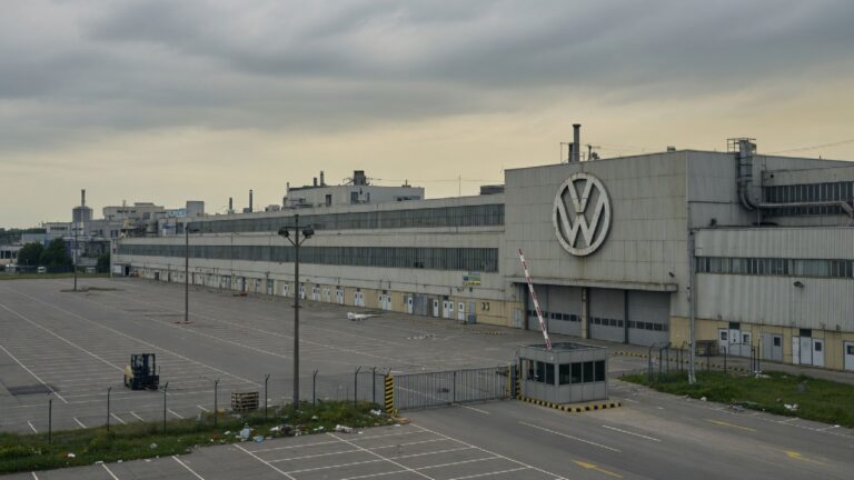 Fábrica da Volkswagen com portões fechados e estacionamento vazio, simbolizando possíveis cortes de empregos e fechamento de plantas industriais