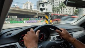 Motorista ao volante de carro moderno com painel de instrumentos visível e radar de trânsito ao fundo, representando infrações de trânsito