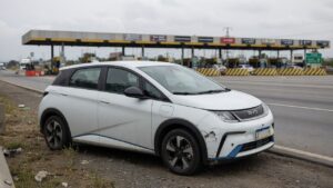 BYD Dolphin elétrico estacionado no acostamento de rodovia brasileira com danos visíveis no para-choque